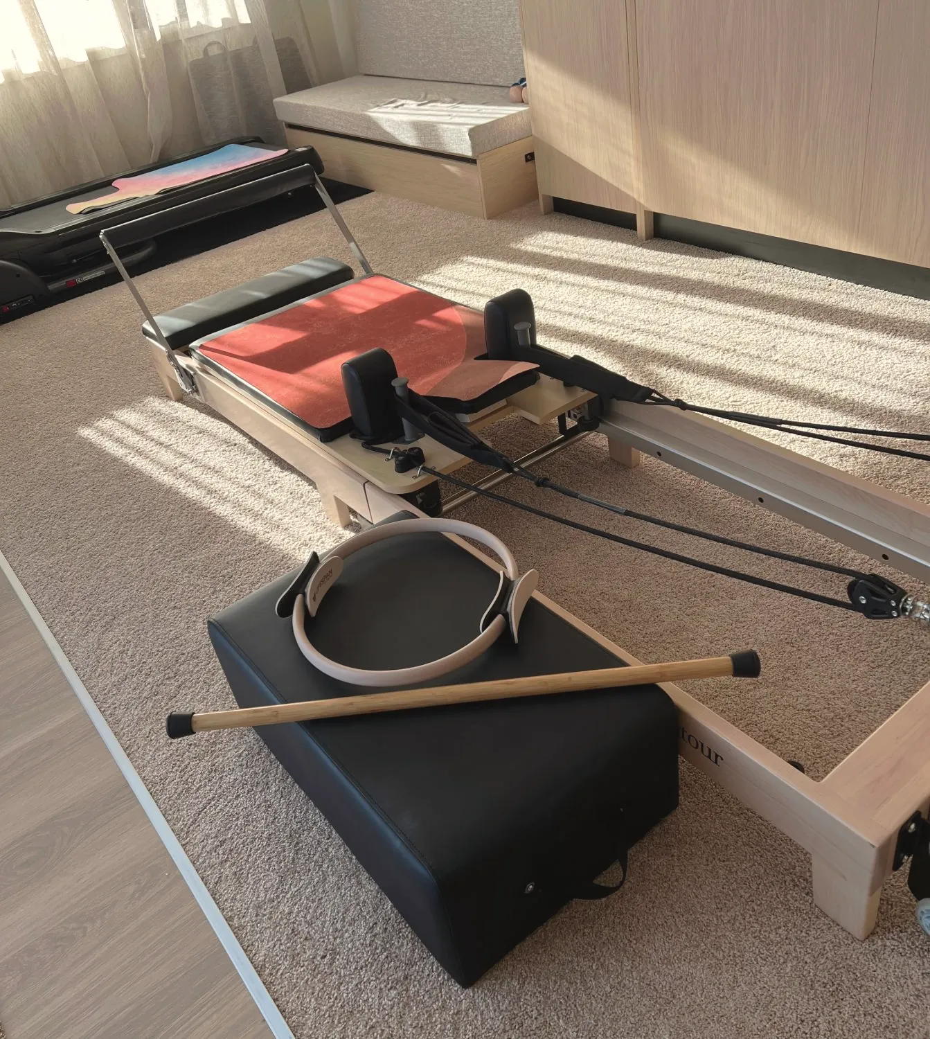 Reformer in the studio with a Pilates ring and stick, afternoon sun across the floor